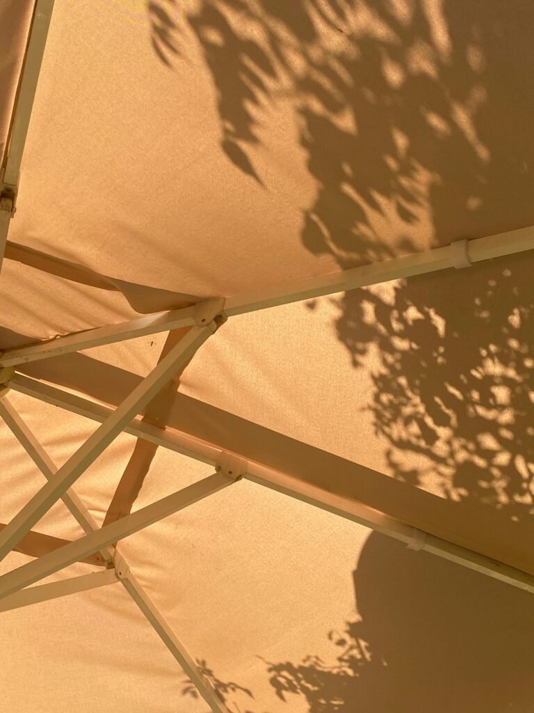 Sunlit garden umbrella with artistic shadow patterns on a warm summer day.