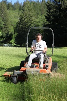 Man using a riding mower to cut grass in a lush, green lawn during a sunny summer day.