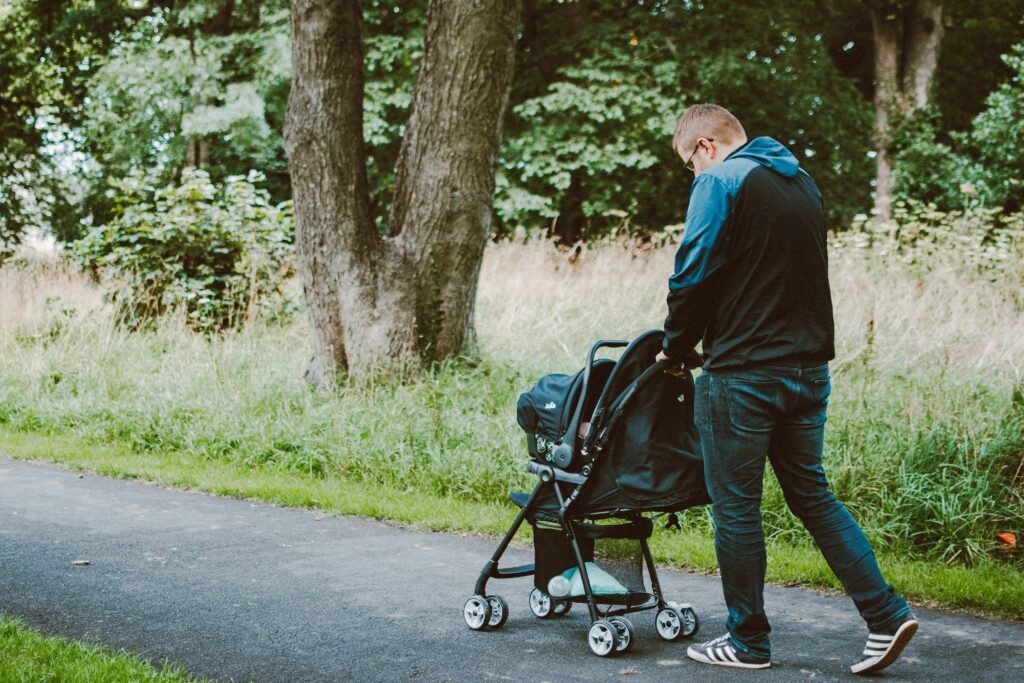 A father pushing a stroller on a park pathway surrounded by nature.