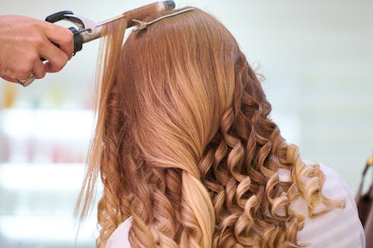 Close-up of a stylist curling blonde hair into glamorous curls at a salon.