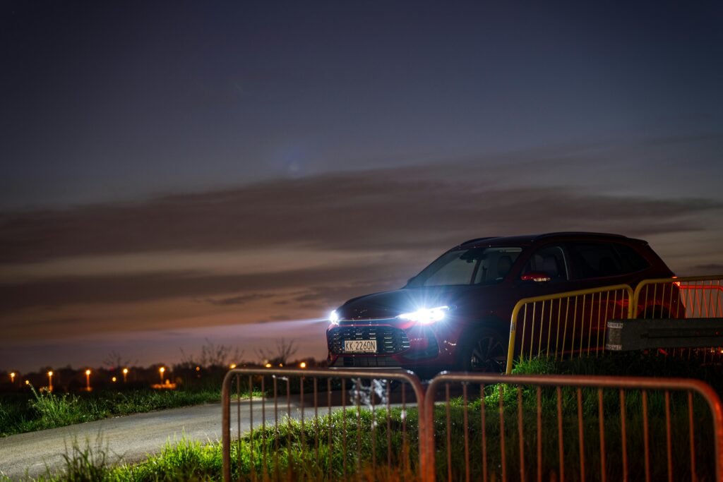 A red SUV with headlights on parked along a rural road at sunset in Kokotów, Poland.