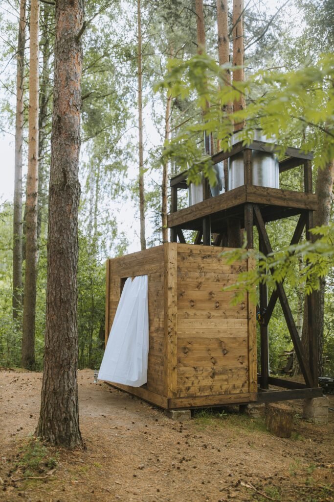 Wooden outdoor shower structure in a serene forest setting, ideal for nature retreats.