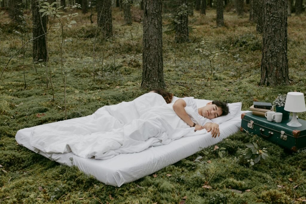 A couple peacefully sleeping on a mattress in a forest setting, capturing a serene outdoor camping vibe.