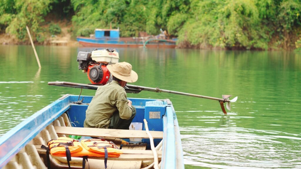 A man in a hat operating a motorboat on a tranquil lake surrounded by greenery.