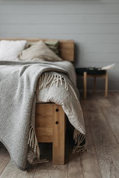 A cozy bedroom with a wooden bed, pillows, and a patterned blanket on a wooden floor.