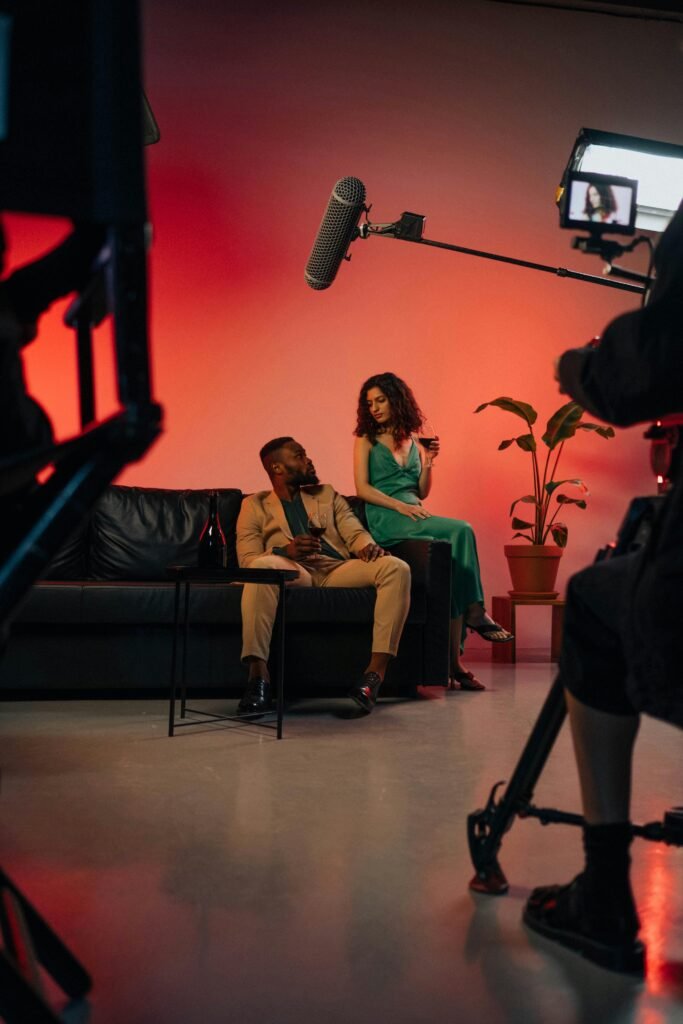 A stylish couple relaxes on a film set, captured with vibrant lighting and a professional film crew.