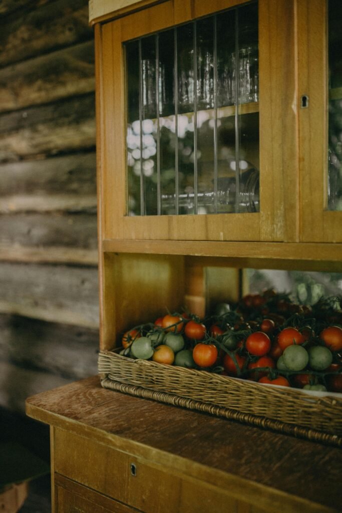 A vintage wooden cabinet filled with ripe tomatoes and glassware in a rustic setting.