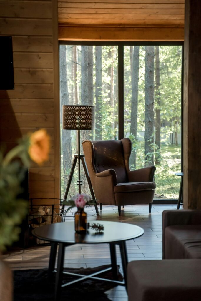 Elegant armchair and lamp in a cozy wooden cabin with forest view.