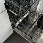 A clean and empty stainless steel dishwasher open in a modern kitchen setting.